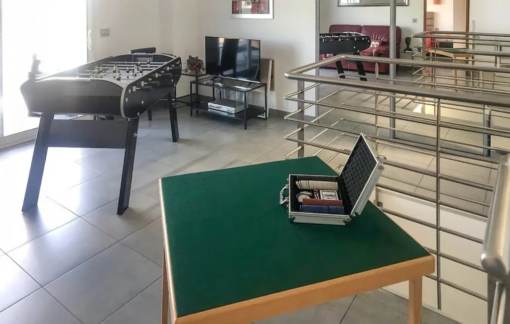 Una sala de juegos con futbolín, televisor y una mesa verde.