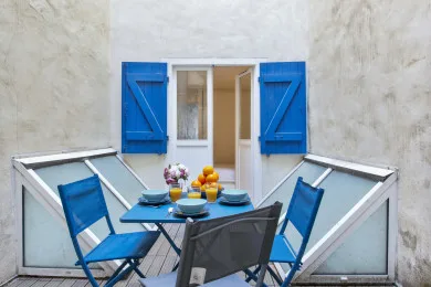 An outdoor dining area with blue seating beside a window with bright blue shutters.