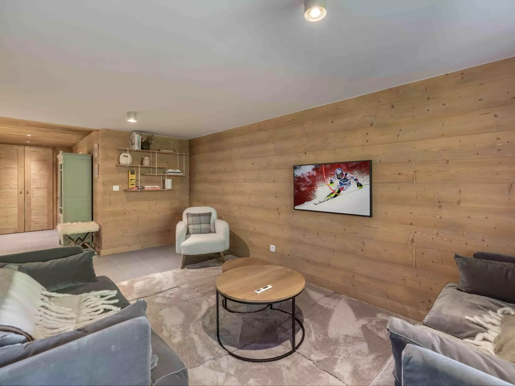 A wood-paneled living room with seating, a coffee table, and a wall-mounted television.