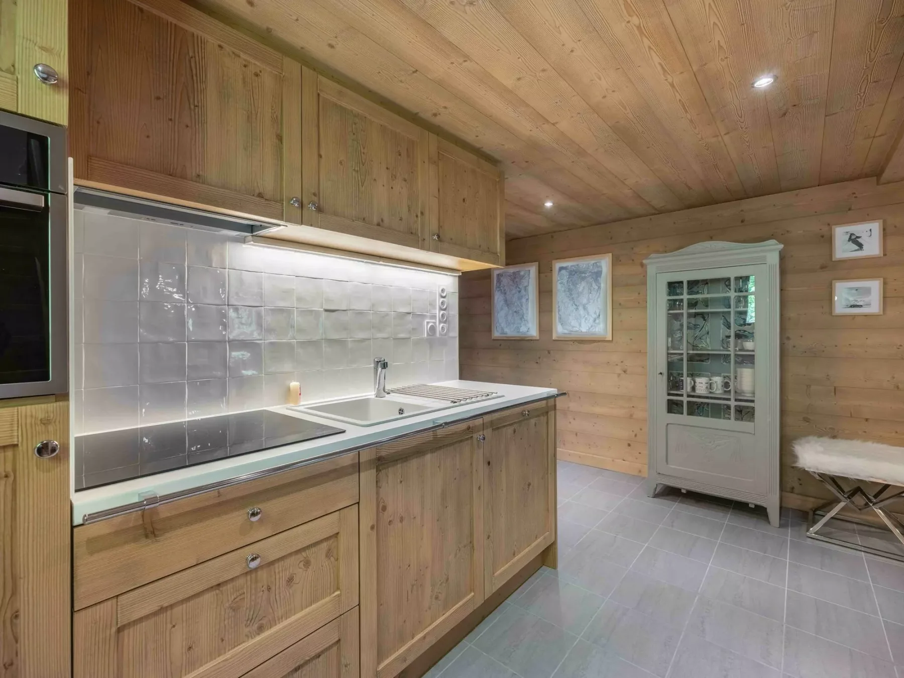 Una cocina revestida de madera con salpicadero de azulejos y un armario con puertas de vidrio.