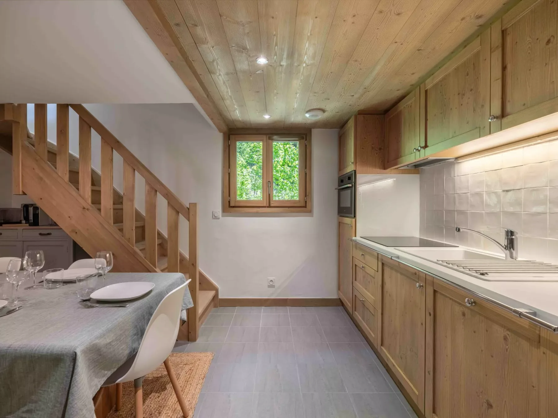 Una cocina compacta con comedor, gabinetes de madera y una mesa junto a la escalera.