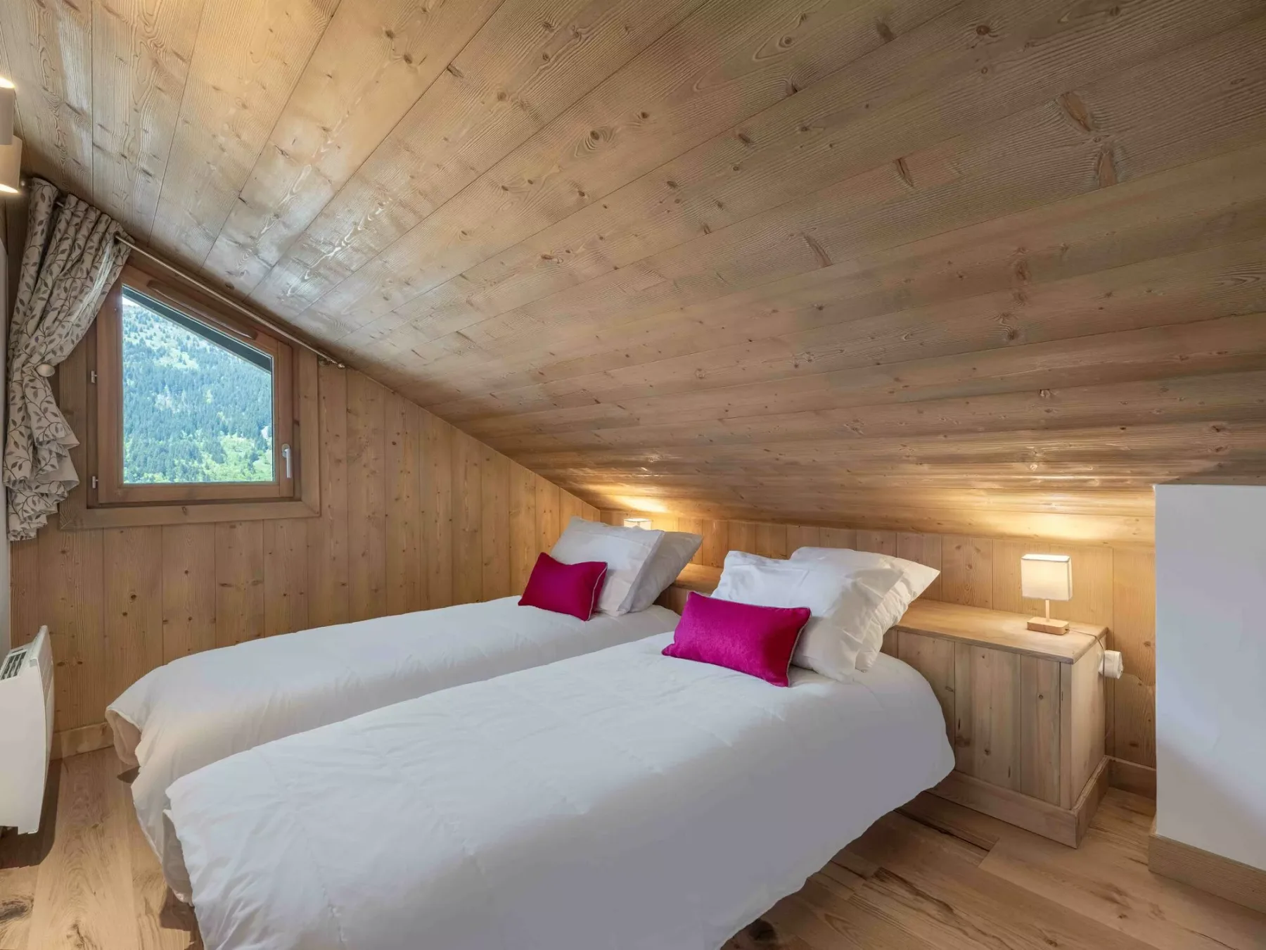 Un dormitorio revestido de madera con dos camas y una ventana pequeña con vistas a colinas verdes.