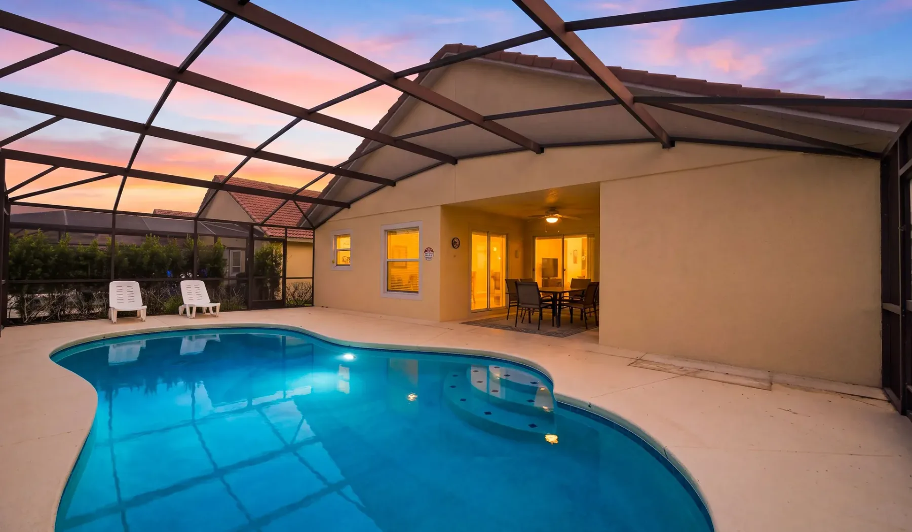 Una piscina junto a un patio y un edificio iluminado al atardecer.