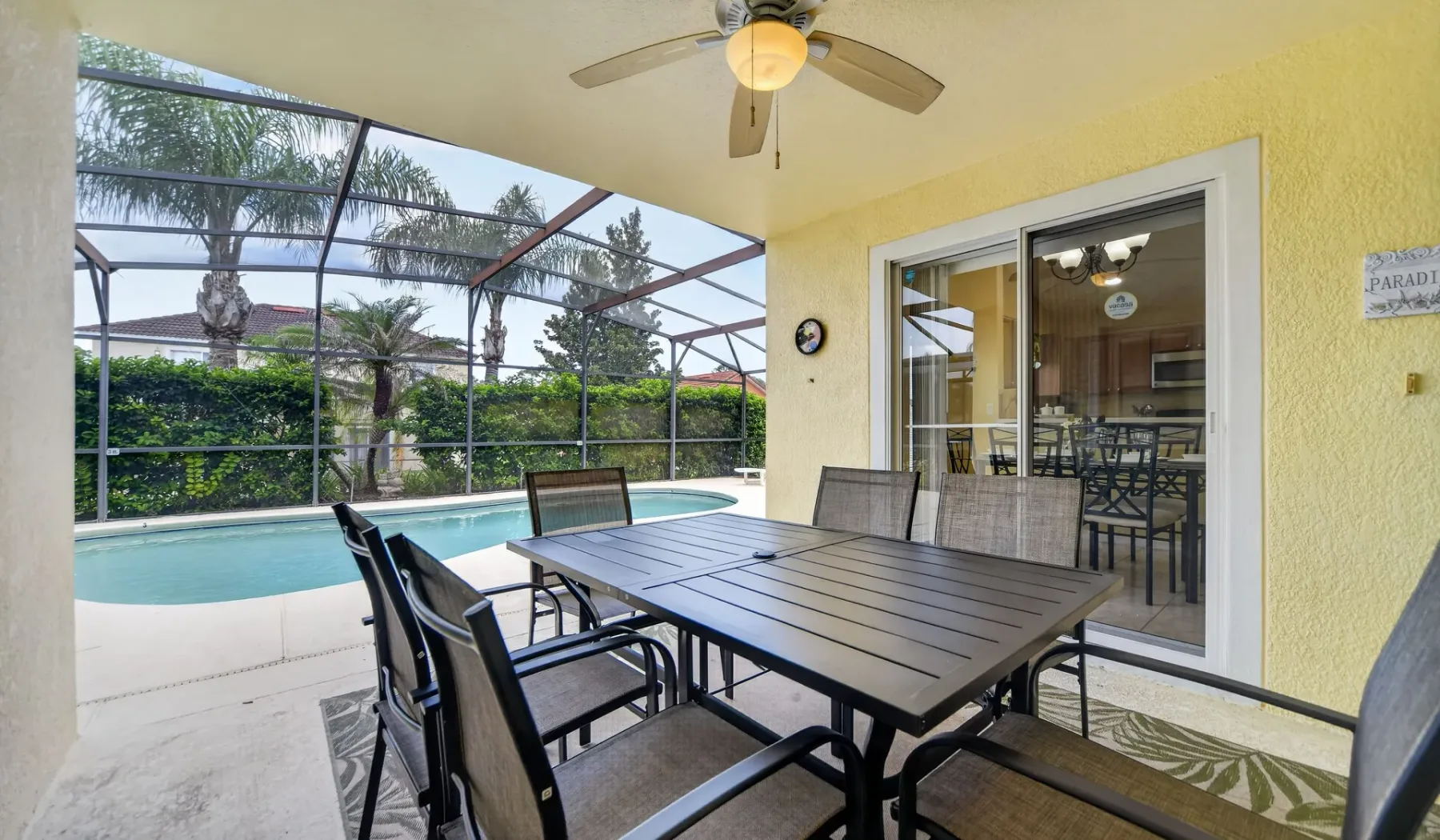 Un patio cubierto con una mesa de comedor da a una piscina y un jardín.