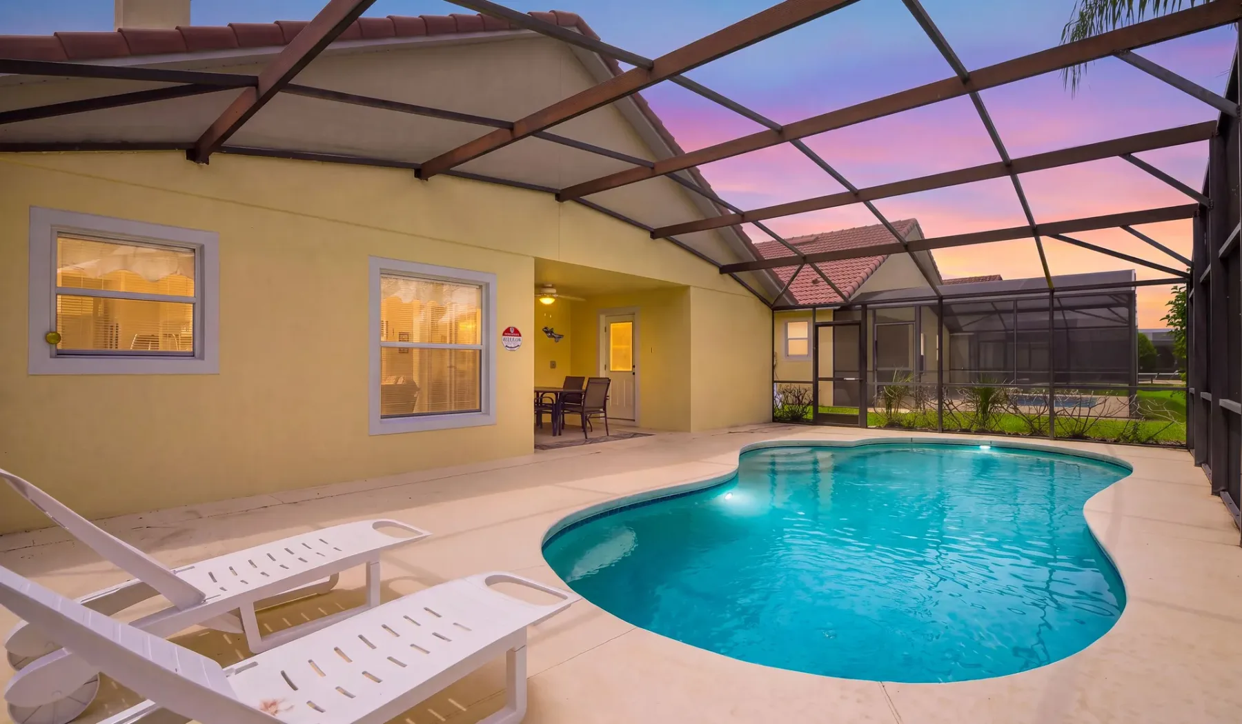 Una piscina está bajo un patio cubierto junto a una casa amarilla.