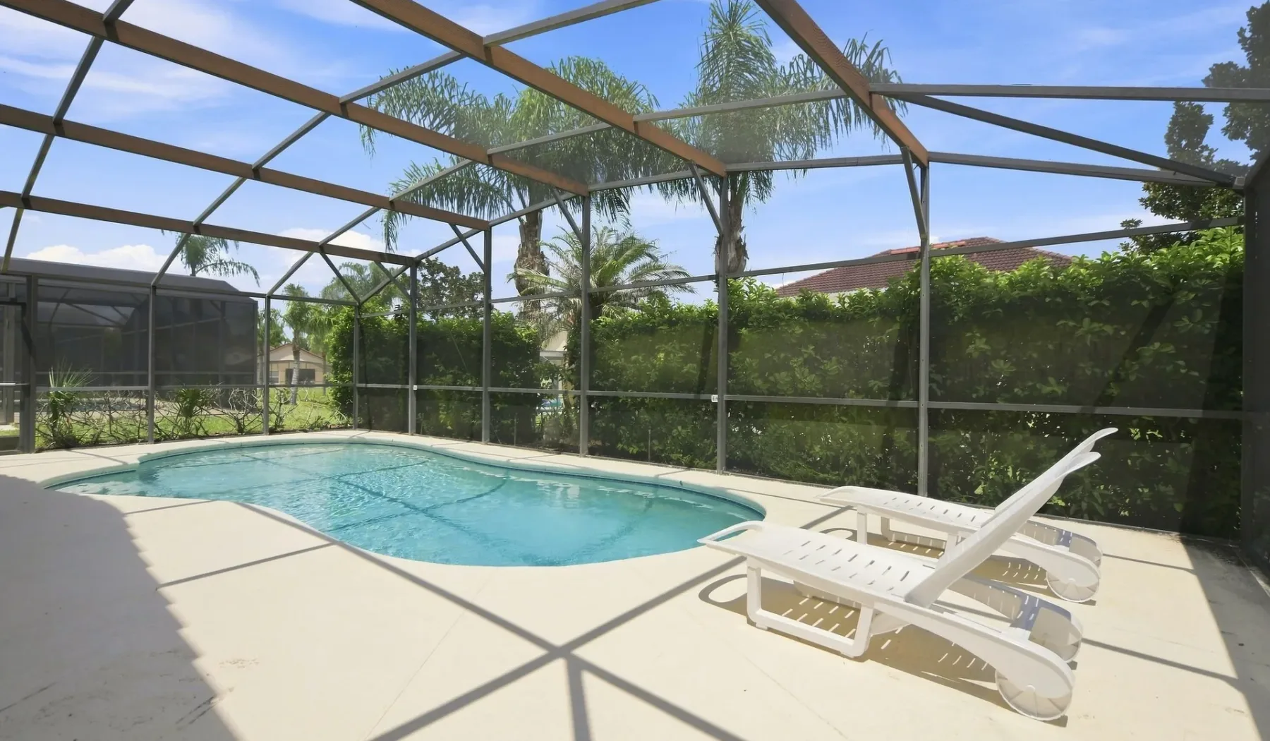 Una zona de piscina exterior con asientos reclinables y vegetación alrededor.
