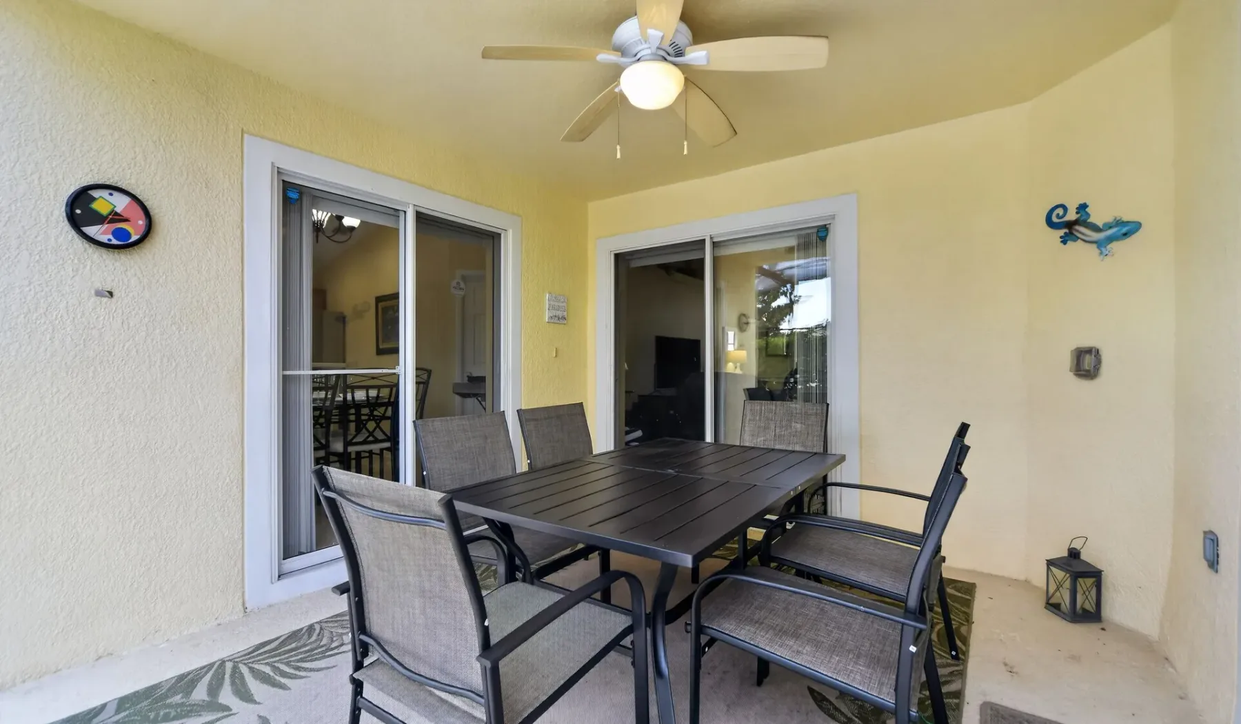 Un patio cubierto con mesa de comedor y asientos bajo un ventilador de techo.