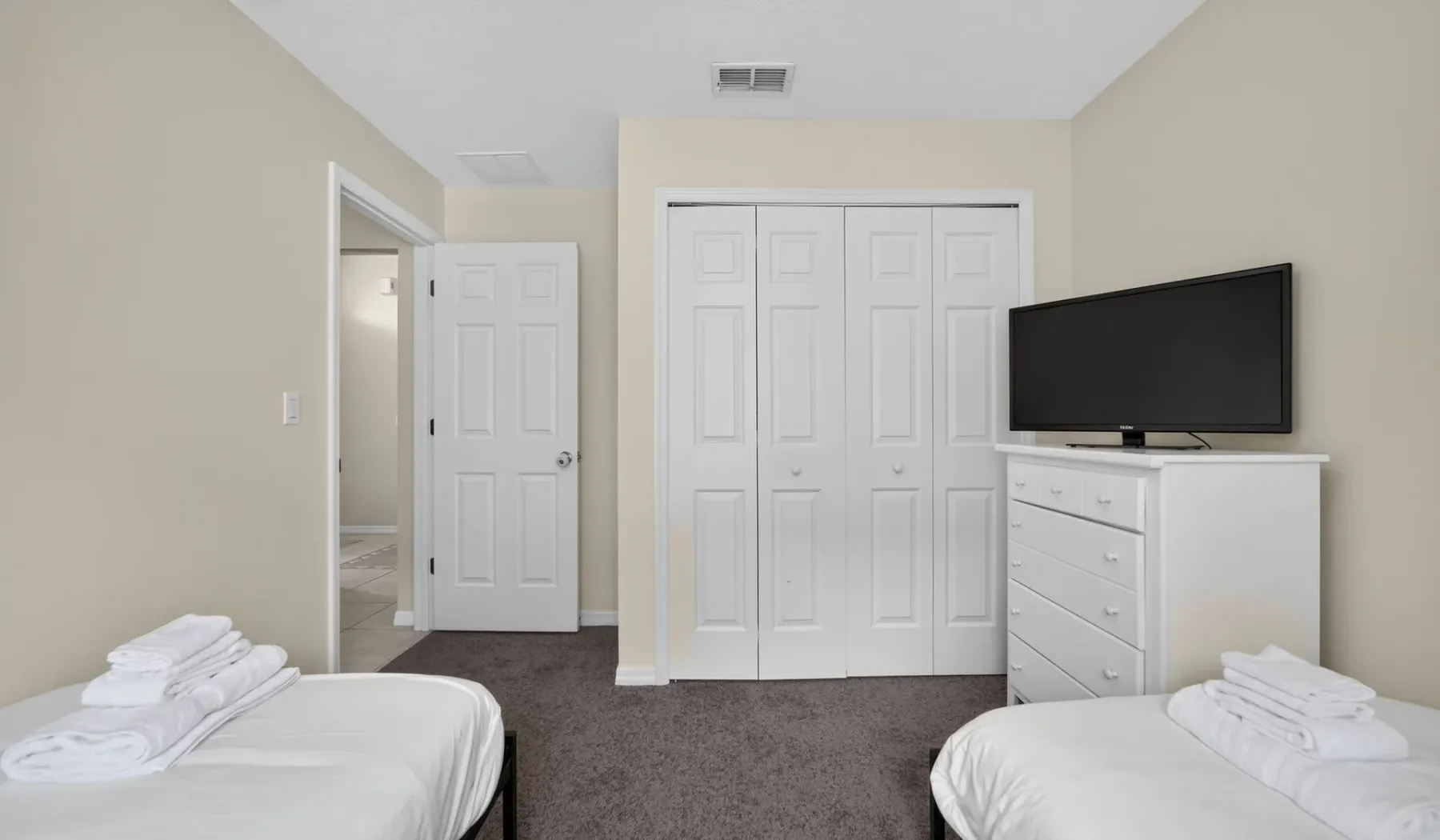 Un dormitorio con dos camas, puertas de armario y un televisor sobre una cómoda.