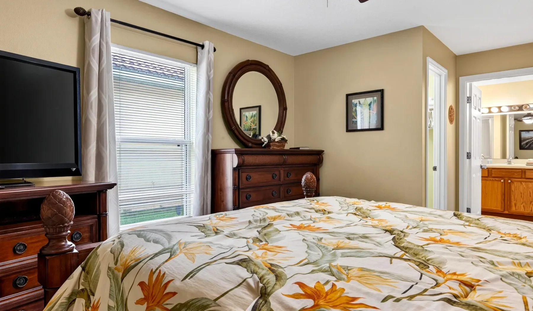 Un dormitorio con una colcha floral, cómodas de madera y un televisor.