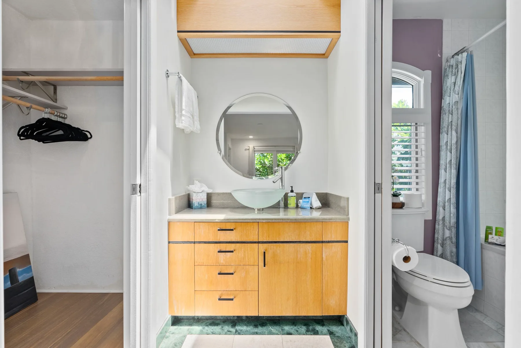 A bathroom vanity with a round mirror, beside a toilet and shower curtain.