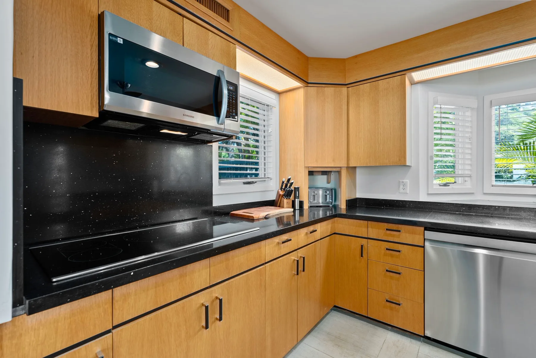 A kitchen with wood cabinets, black countertops, and windows above the sink.