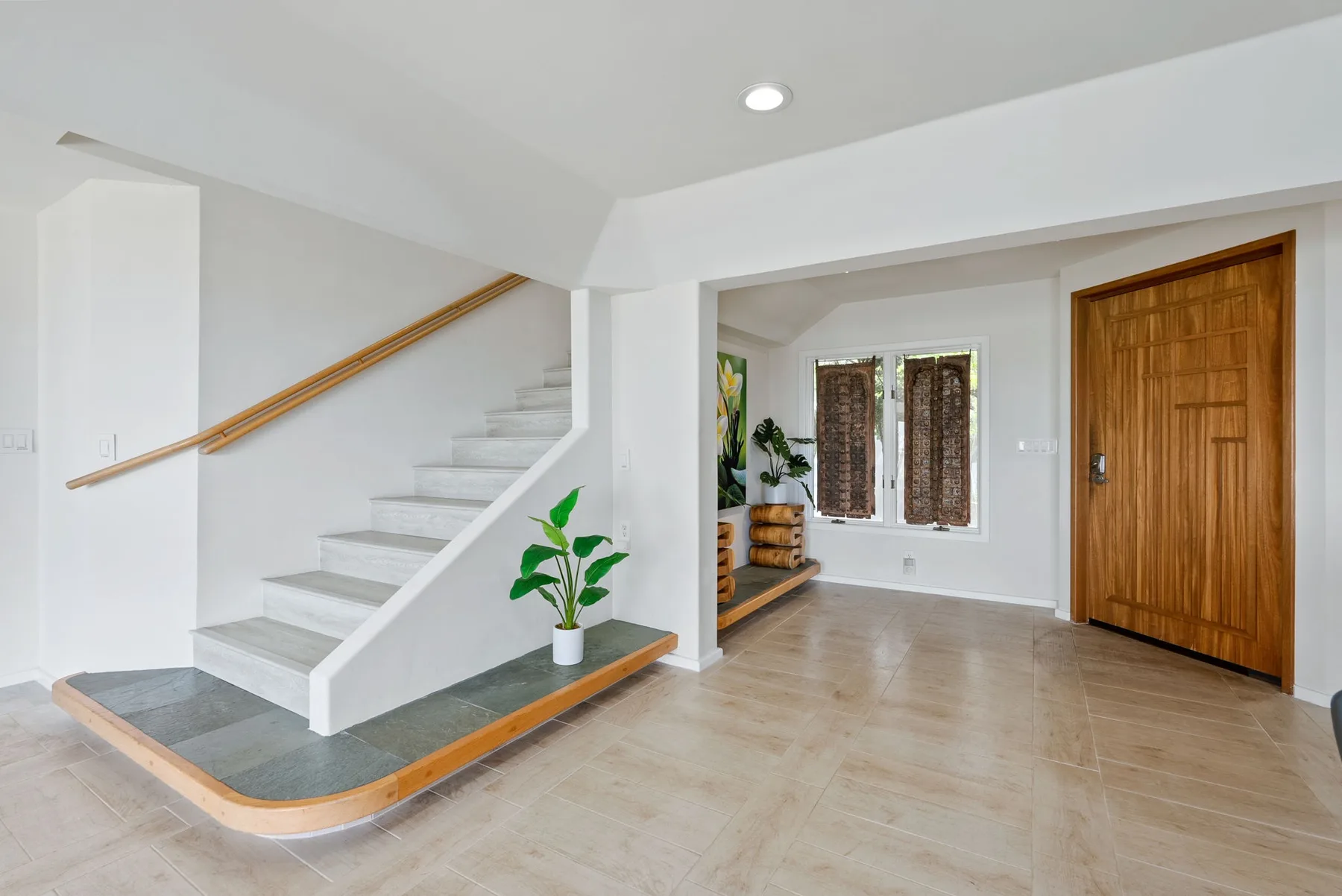 An interior entry hall with a staircase, wooden door, and potted plant.
