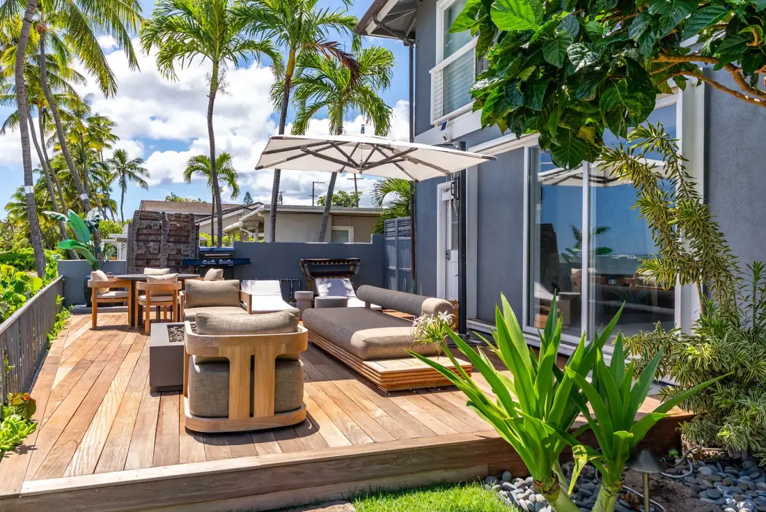 A sunny outdoor deck has cushioned seating beneath a large umbrella.