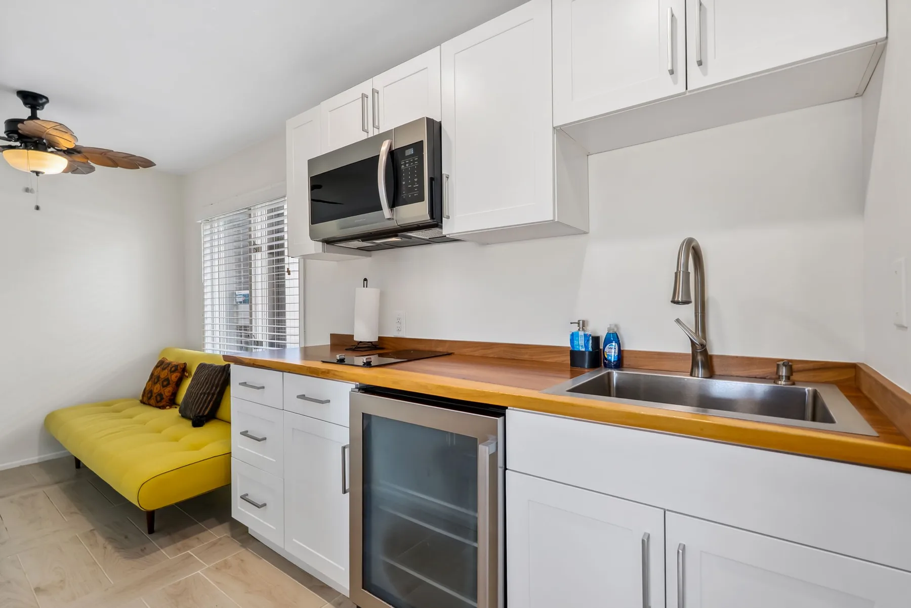 A compact kitchen with white cabinets, a wood countertop, and a yellow sofa nearby.