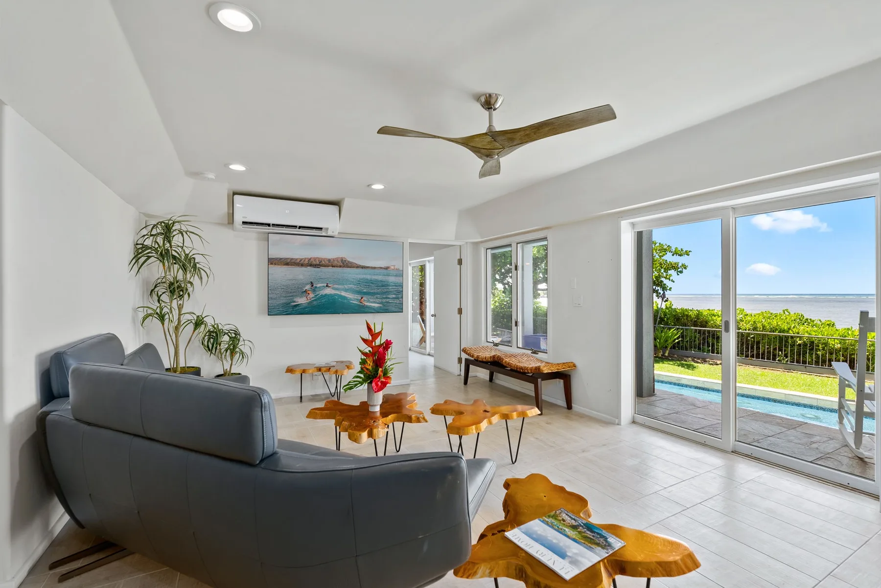 A bright living room opens onto a patio with a pool and ocean view.