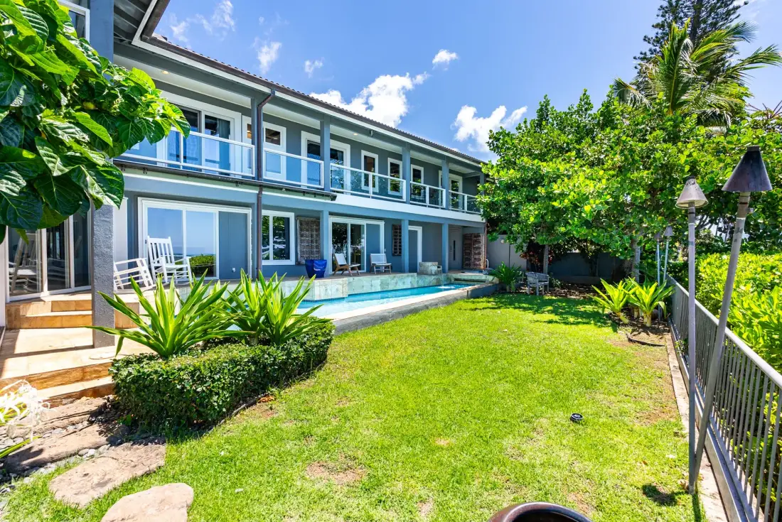 A two-story building overlooks a swimming pool and a grassy garden.