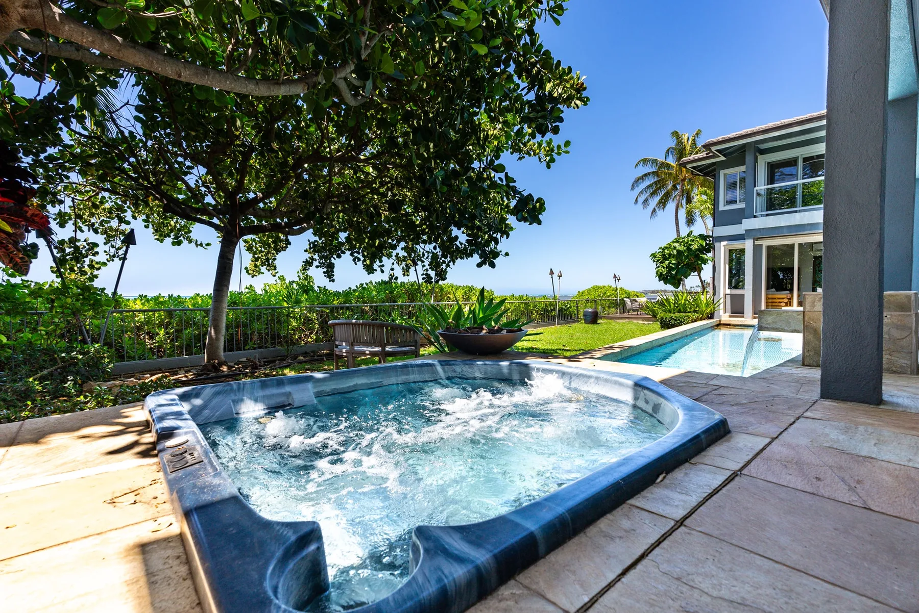 An outdoor pool and bubbling spa sit beside a modern house.