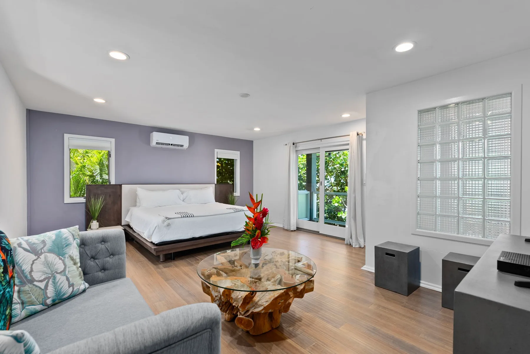 A bright bedroom and sitting area with a bed, seating, and a glass coffee table.