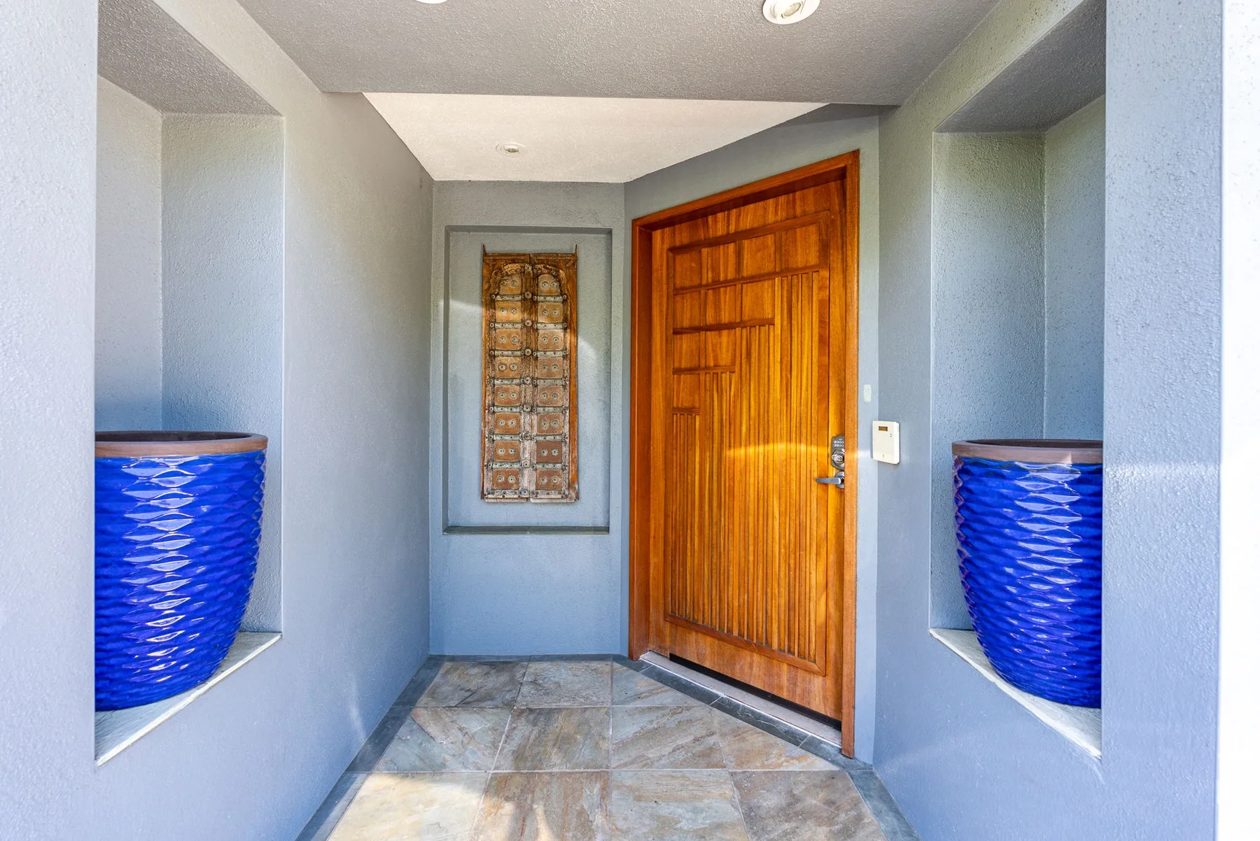 A recessed entryway with a wooden door and patterned tile floor.
