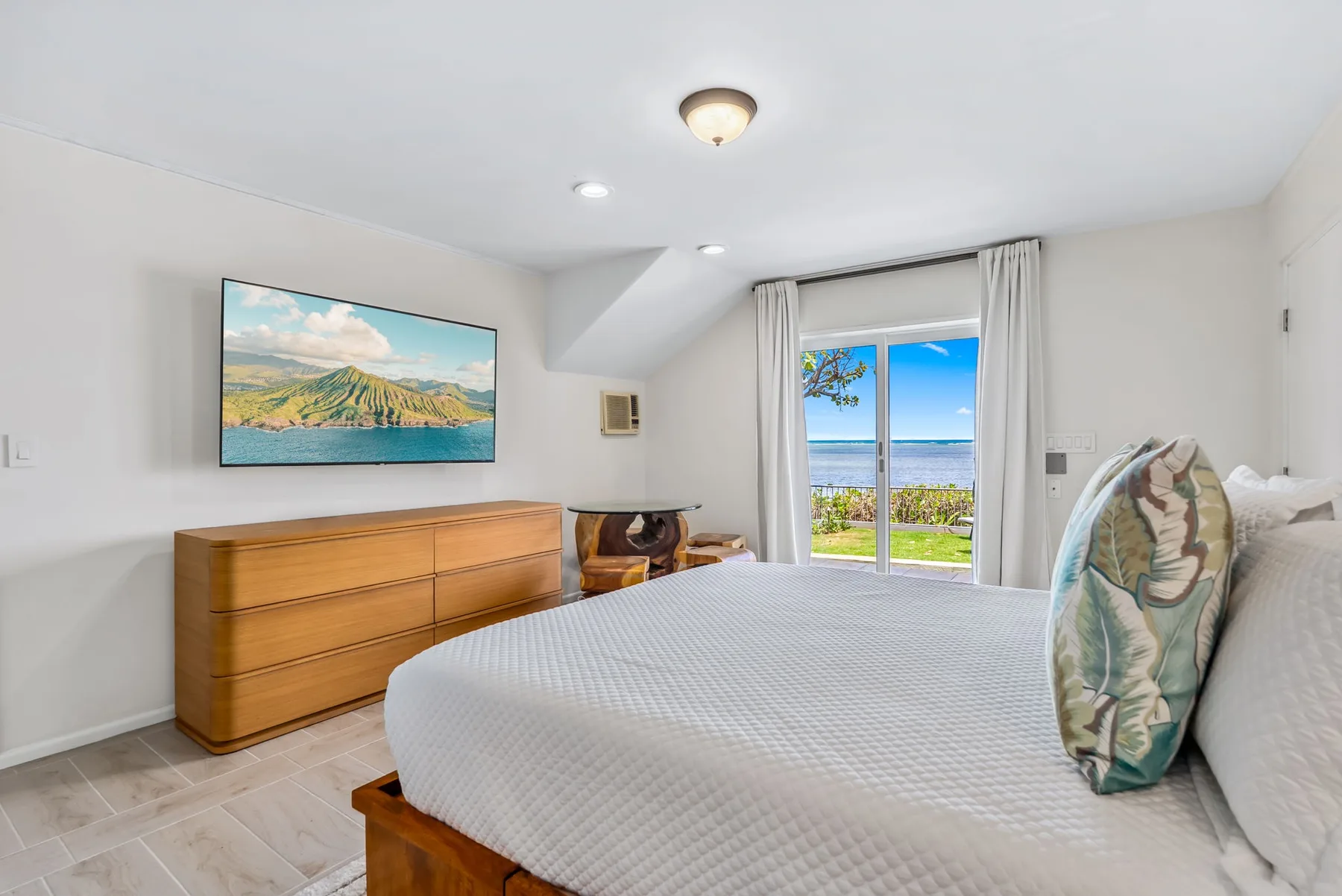 A bedroom with a bed, wooden dresser, and sliding glass doors overlooking the water.