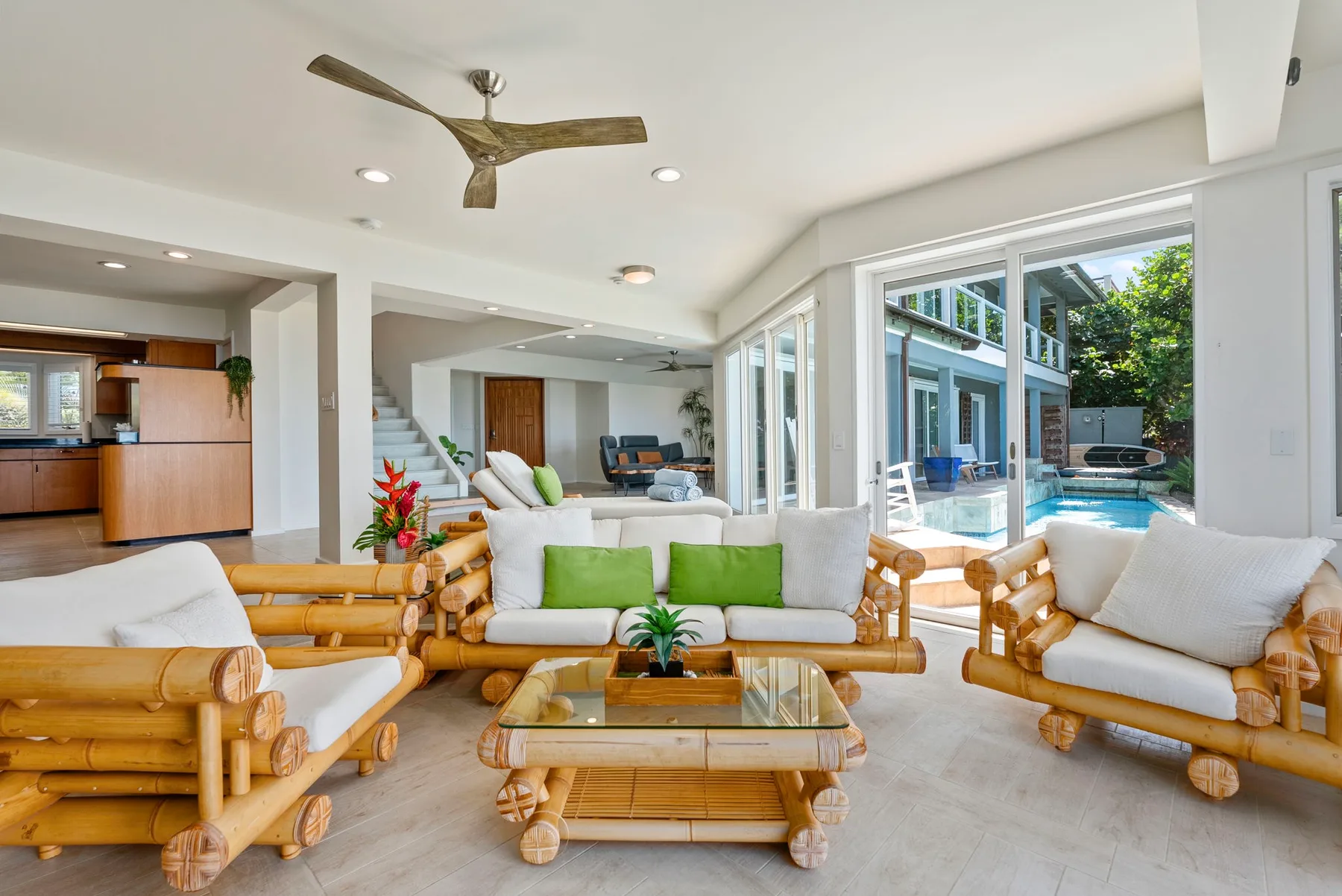 A bright living room with bamboo seating and wide windows overlooking a pool.