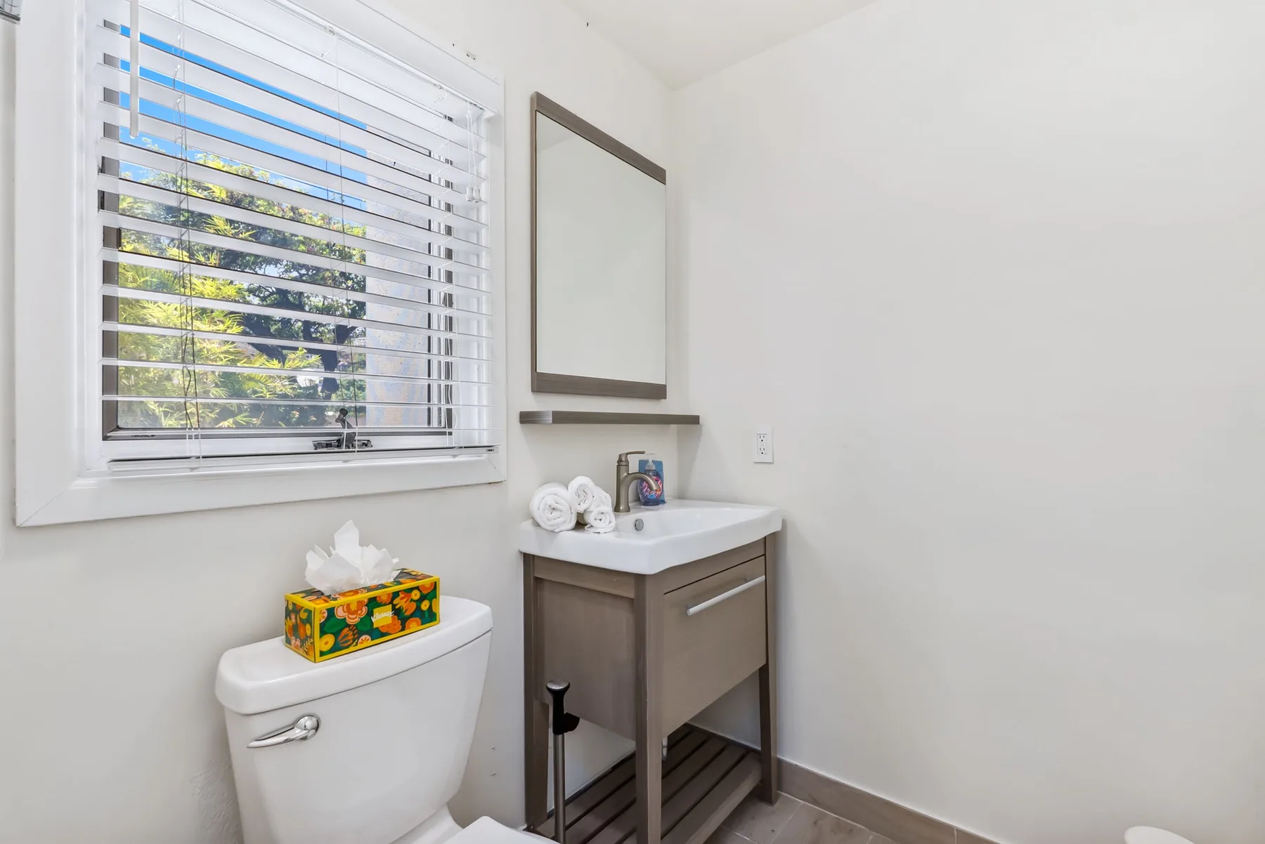 A bathroom with a sink, mirror, and window with blinds.