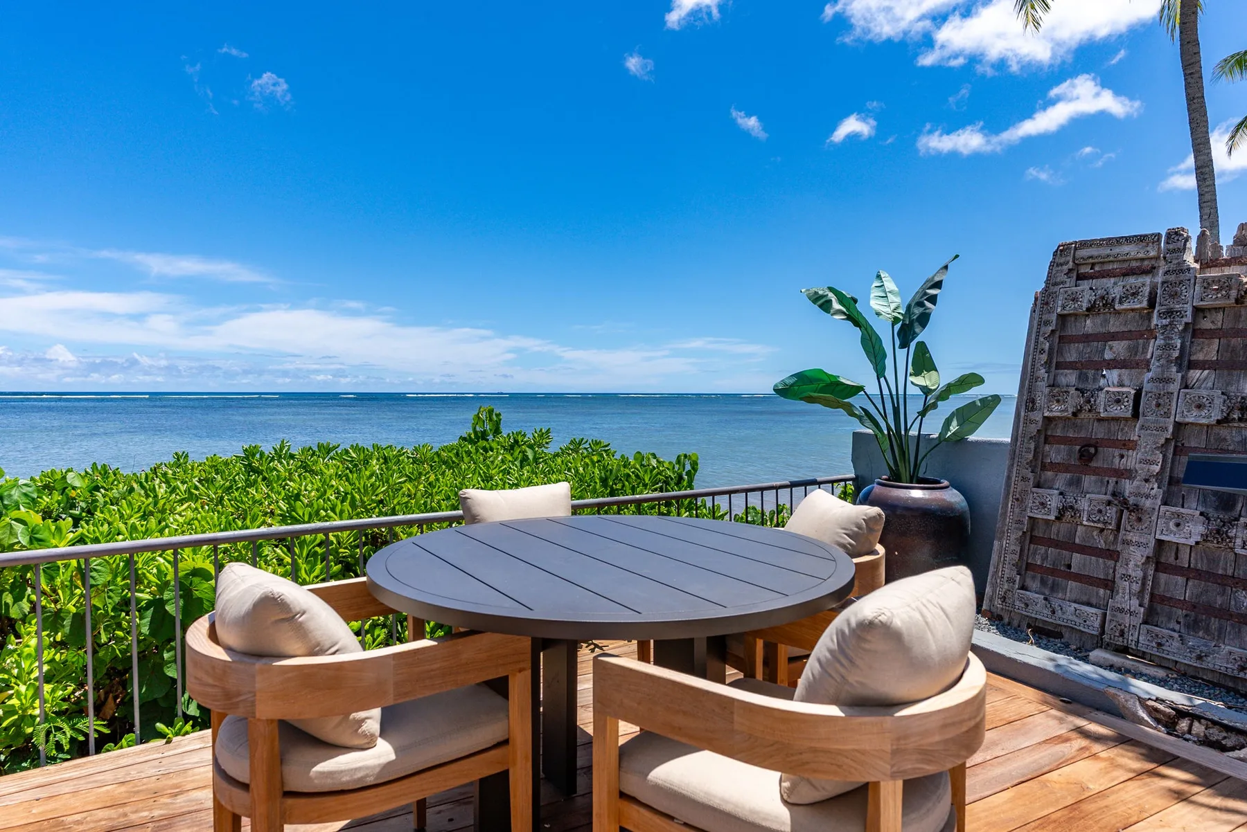 An oceanfront patio has a round table and cushioned wooden seating.