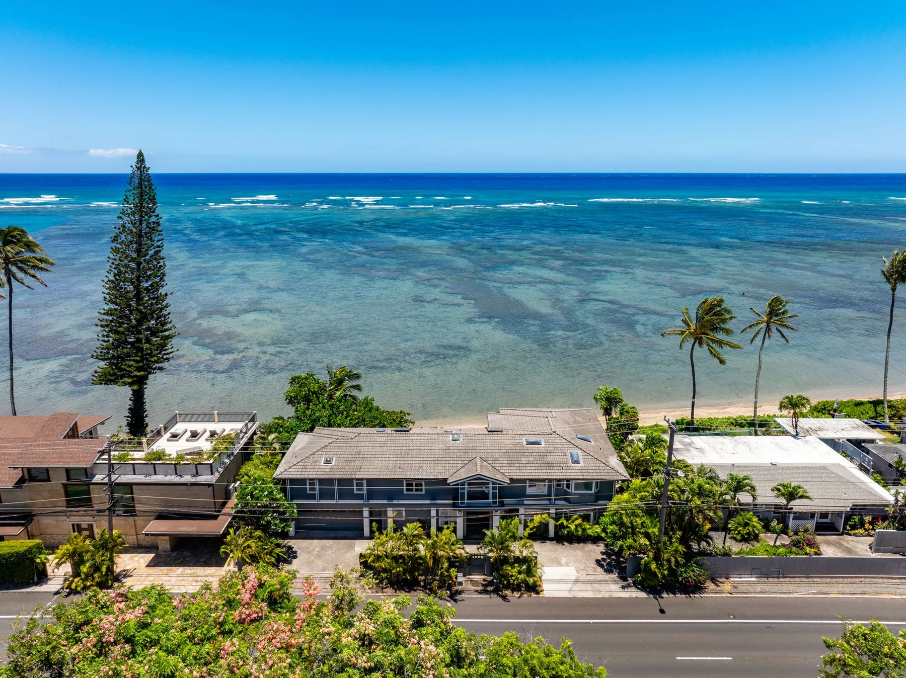 Aerial view of oceanfront homes beside a road and shallow turquoise water.
