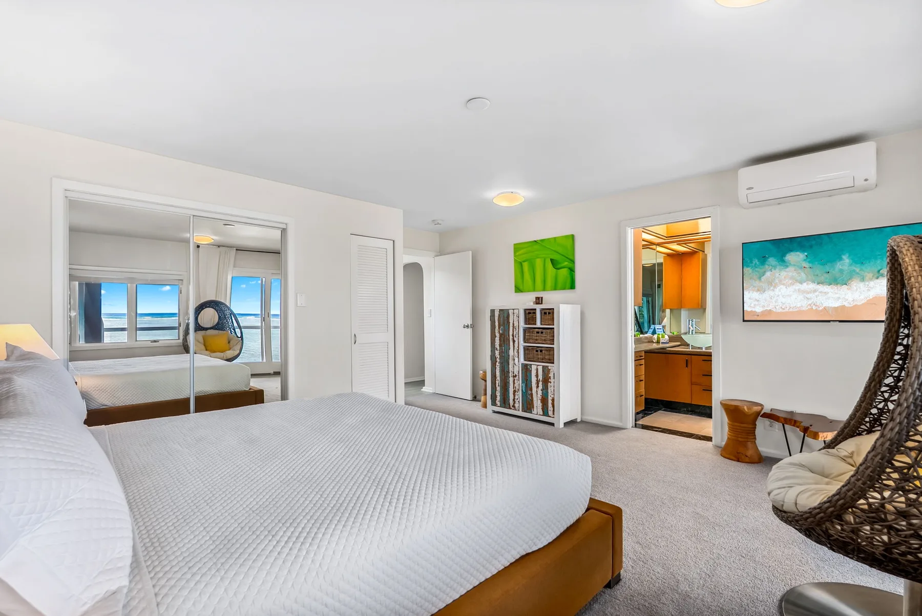 A bedroom with a large bed, mirrored closet doors, and a doorway to the bathroom.