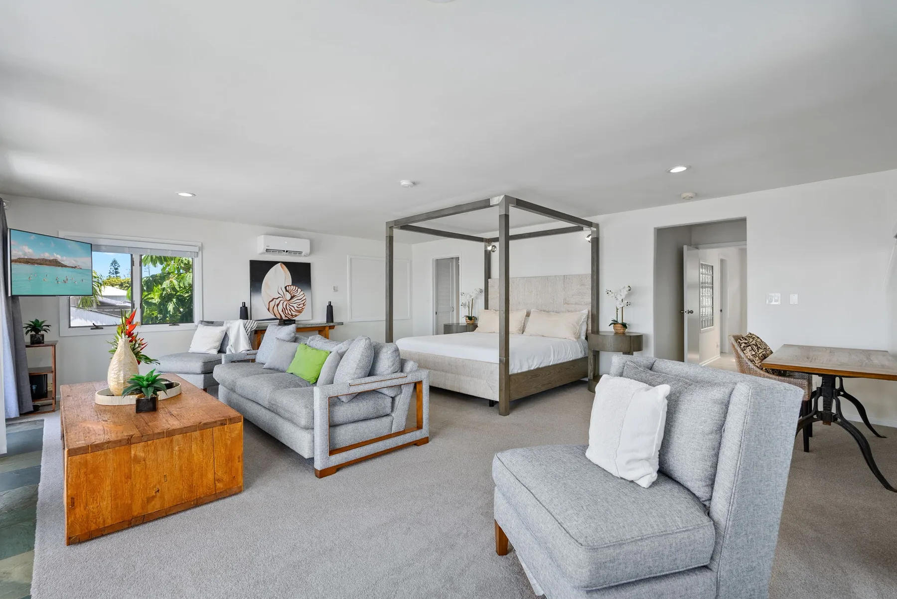An open-plan living and sleeping area features gray seating and a four-poster bed.