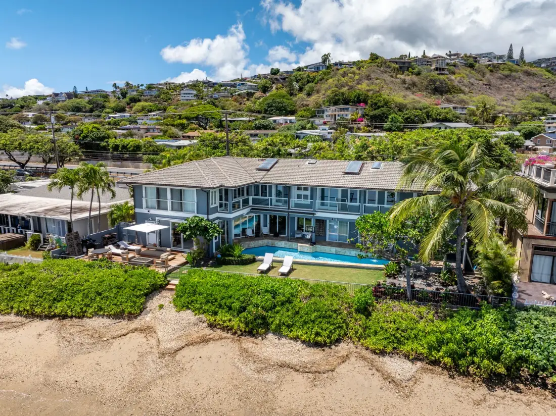 A modern beachfront home with a swimming pool and hillside homes in the background.