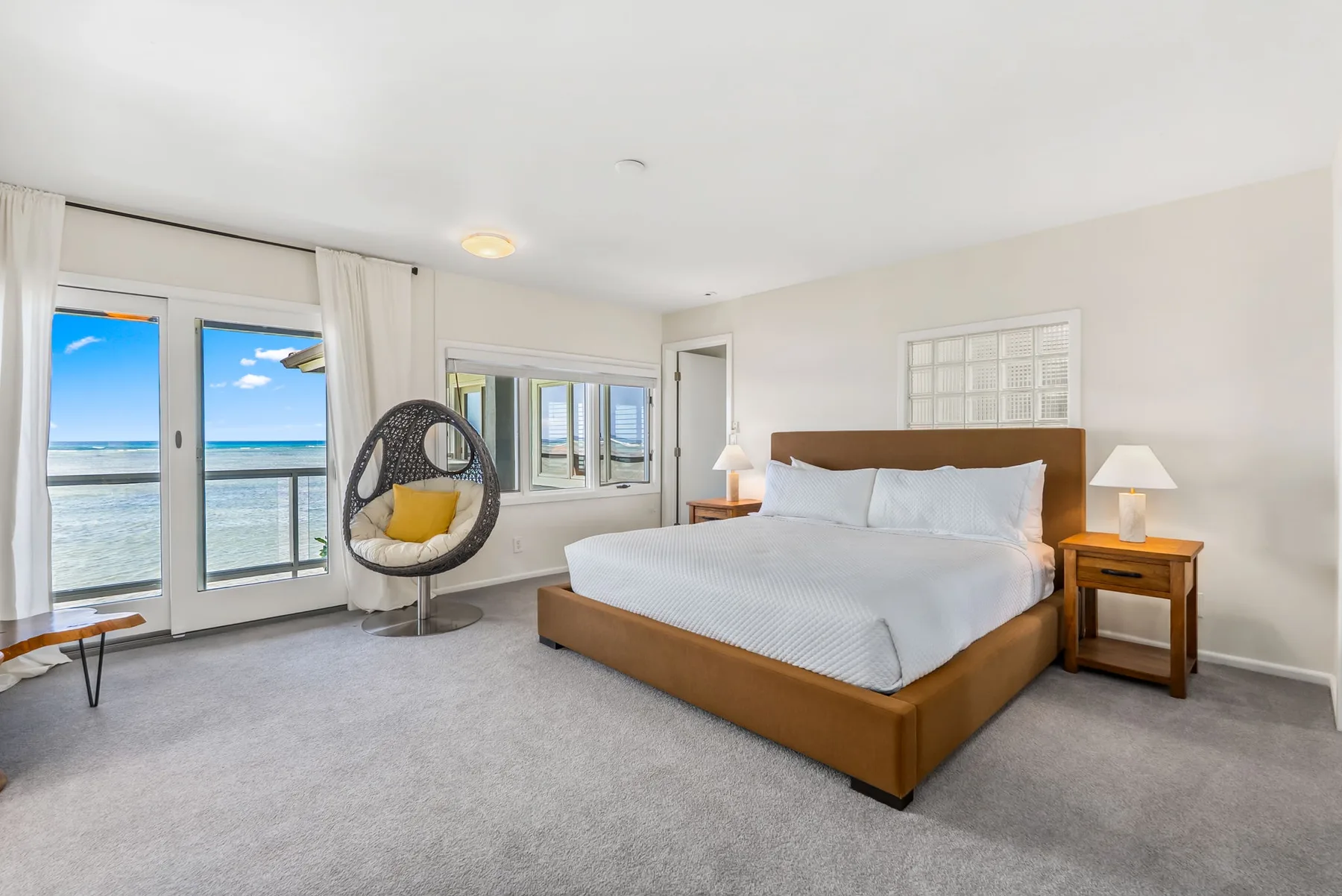 A bright bedroom with a large bed and a hanging chair beside balcony doors.