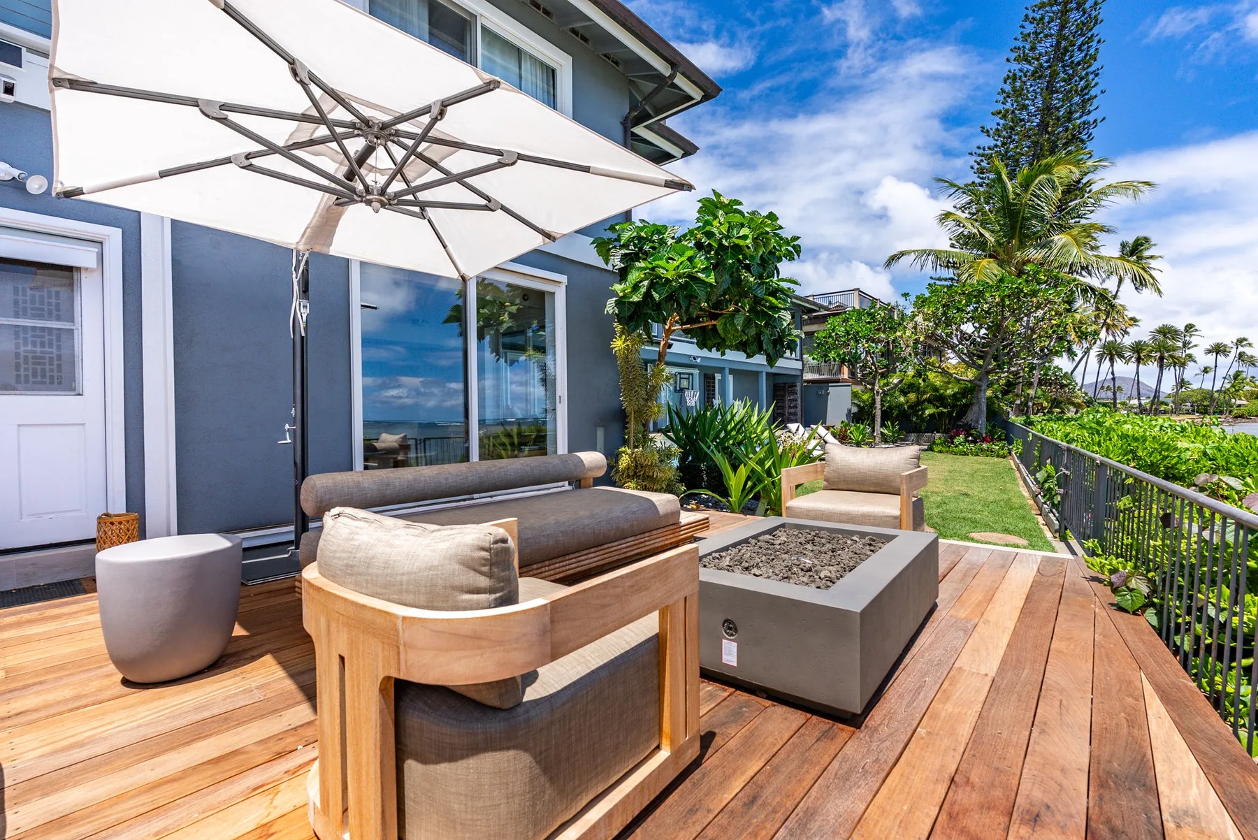 An outdoor deck has seating beside a planter and a large shade umbrella.