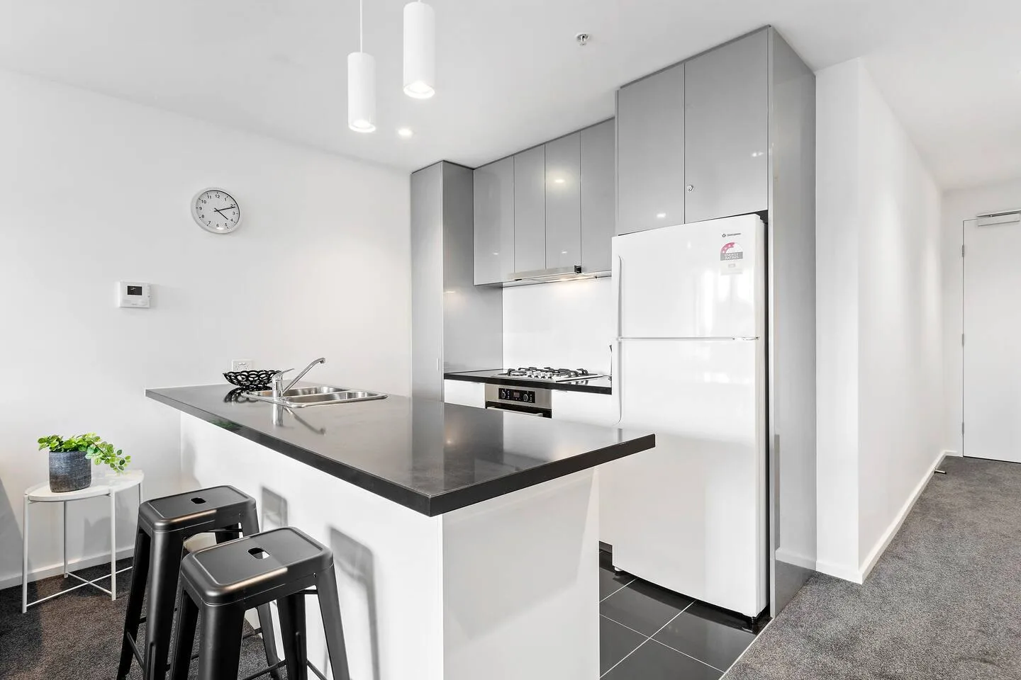 Una cocina luminosa con gabinetes grises, un refrigerador y una barra con asientos.