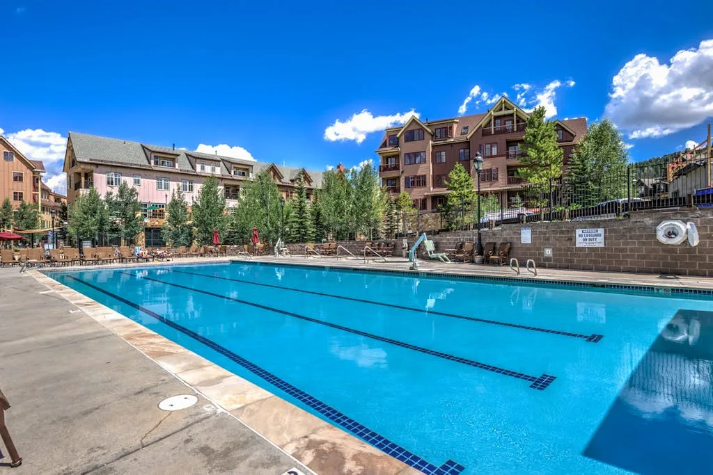 An outdoor swimming pool sits beside multi-story buildings under a clear blue sky.