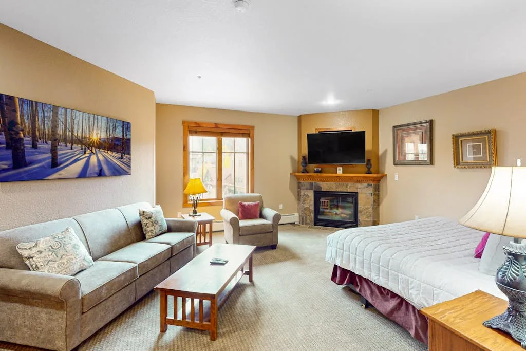 A bedroom with a bed, seating area, and fireplace beneath a wall-mounted television.