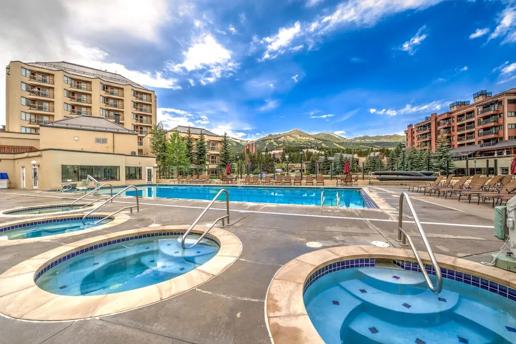 An outdoor swimming pool and round spa pools sit among resort buildings.