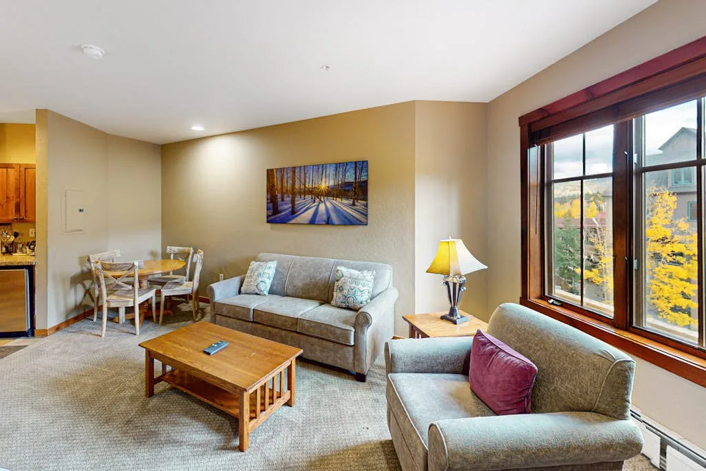 A living room with seating, a coffee table, and a dining area by the window.