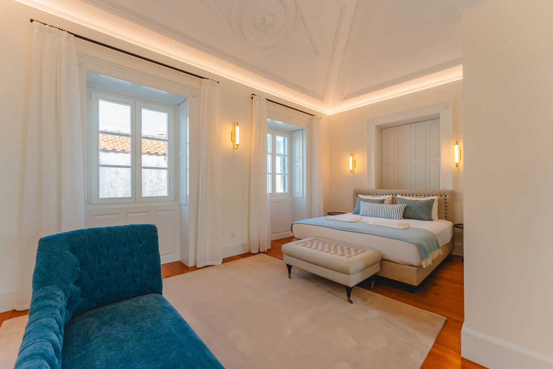 Dormitorio con una cama, un banco tapizado y asientos azules.