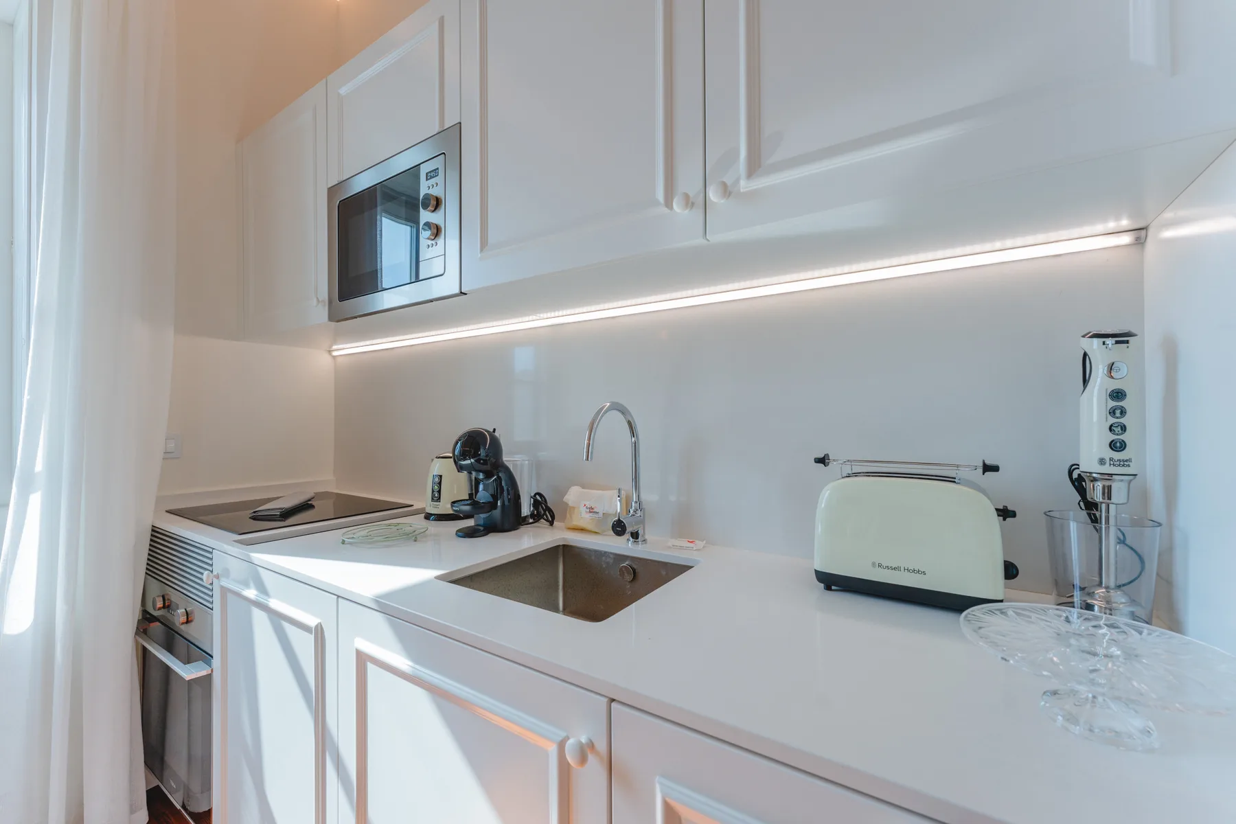 Una cocina luminosa con armarios blancos, una encimera y un fregadero.
