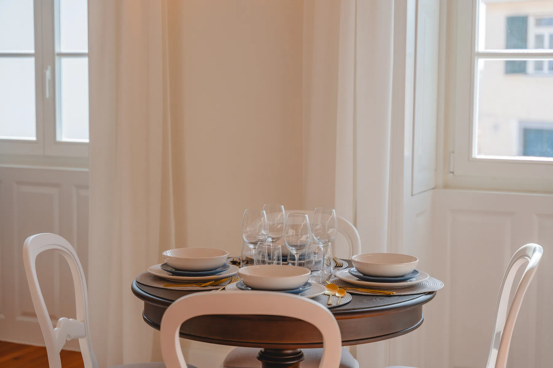 Un comedor con la mesa puesta junto a ventanas altas.