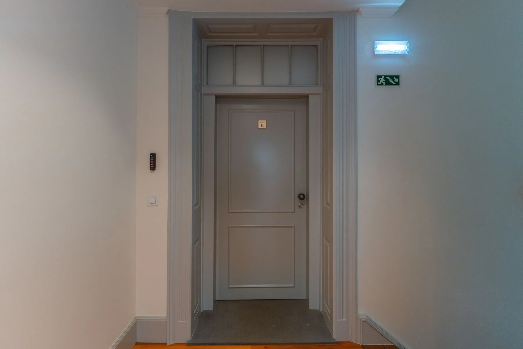 Un pasillo interior con una puerta cerrada y señales de salida iluminadas.
