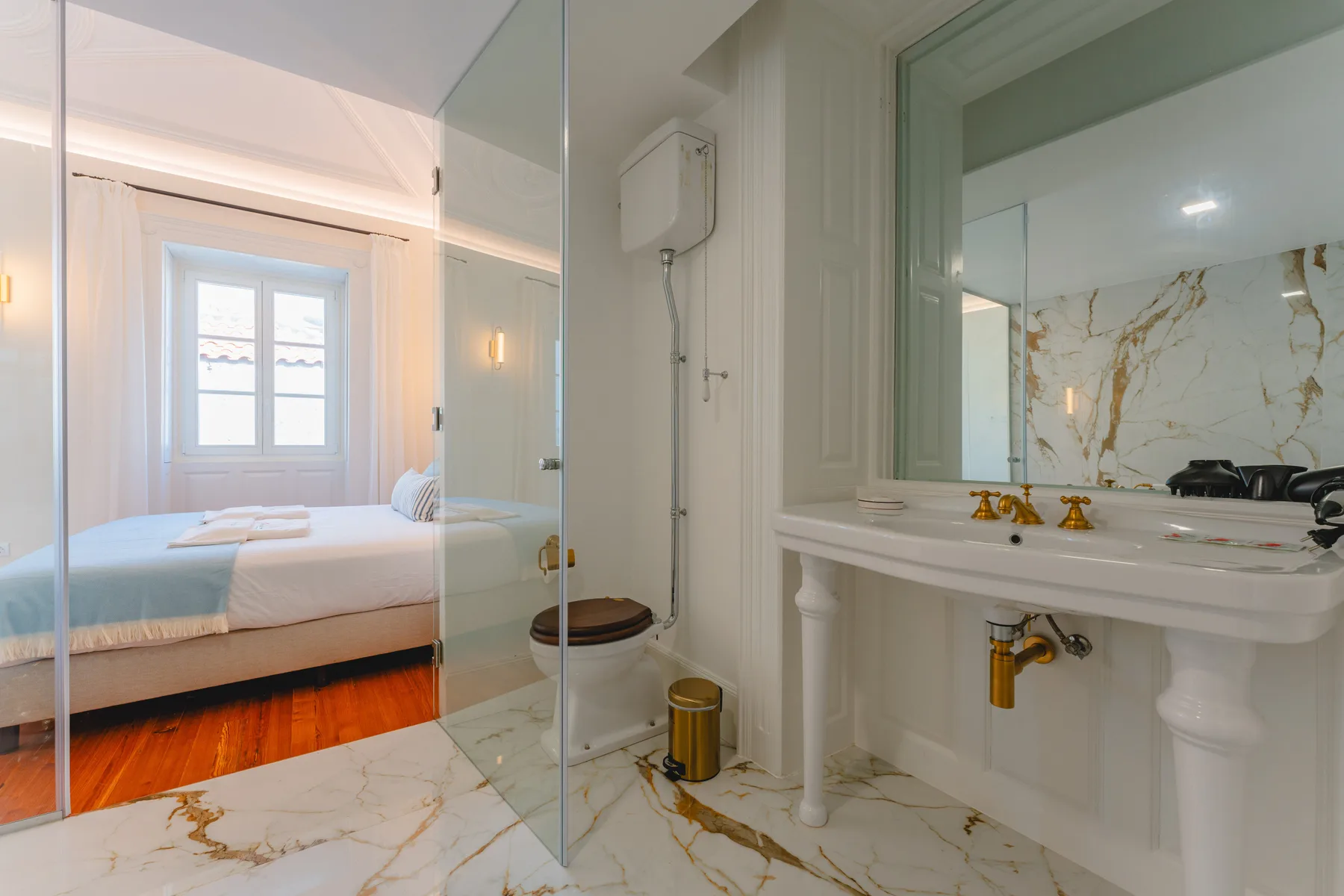 Baño con ducha de vidrio y lavabo, abierto a un dormitorio.