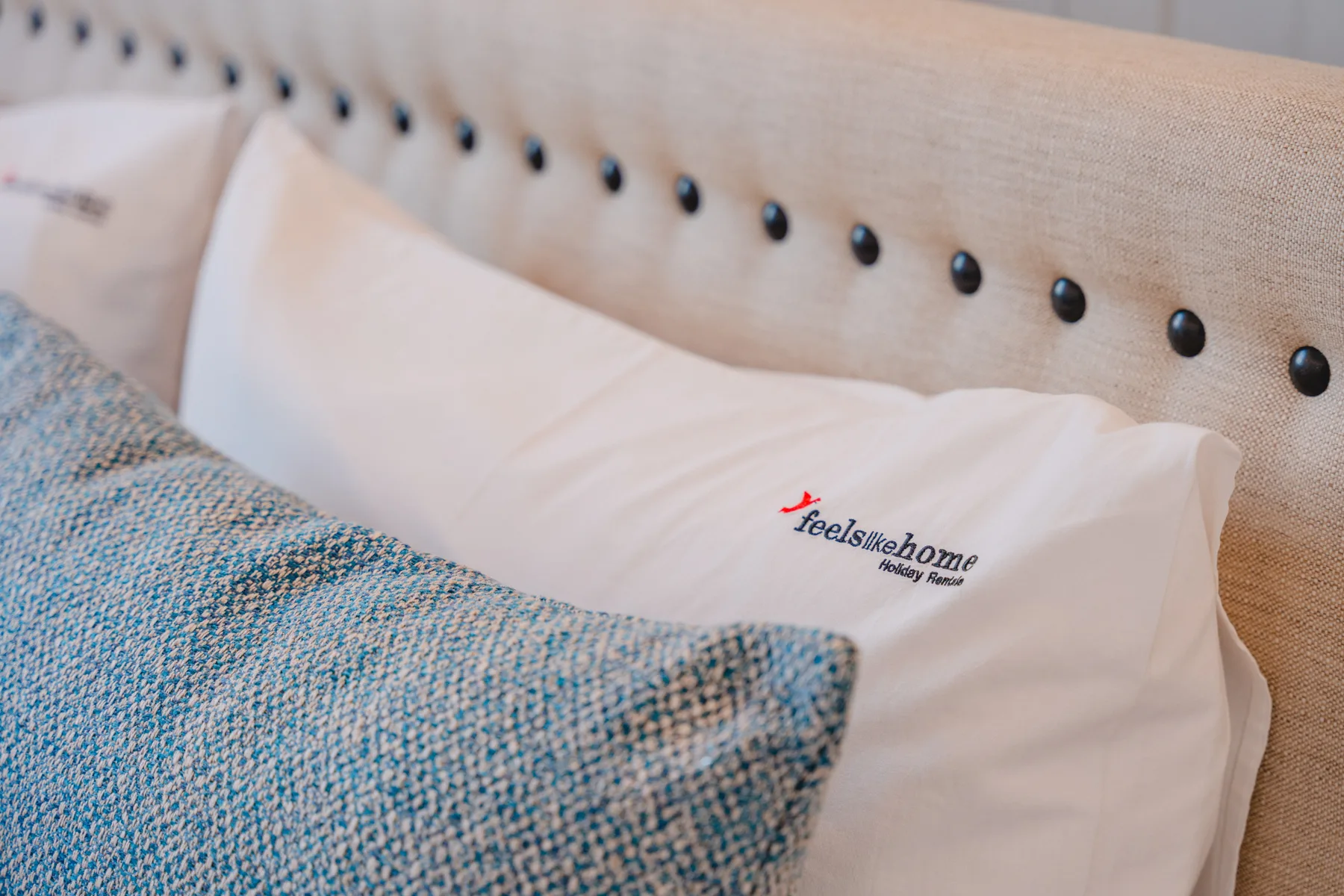 Una cama con almohadas blancas y un cojín azul estampado.