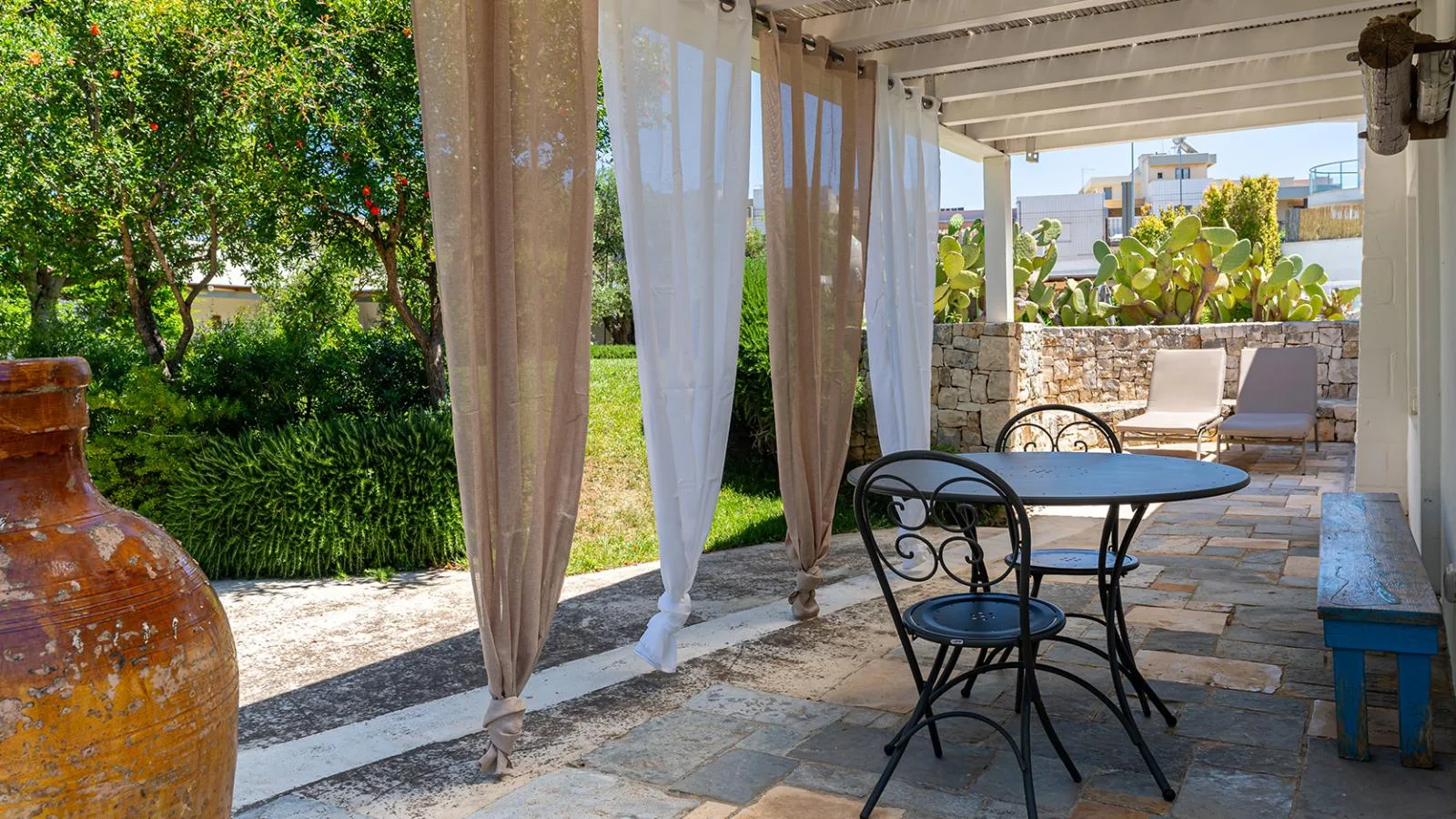 Terraza con una mesa, sillas, plantas y tumbonas de piedra.