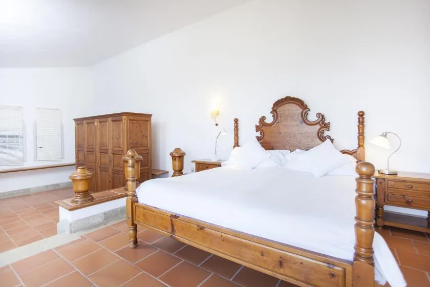 A bedroom with a wooden bed, white bedding, and a wardrobe.