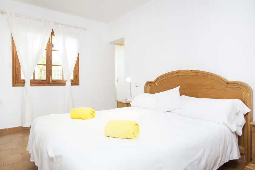 A bright bedroom with white bedding and a wooden headboard.