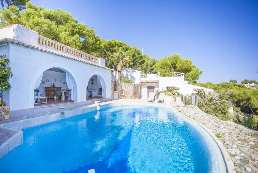 An outdoor swimming pool curves beside a white building with arched openings.