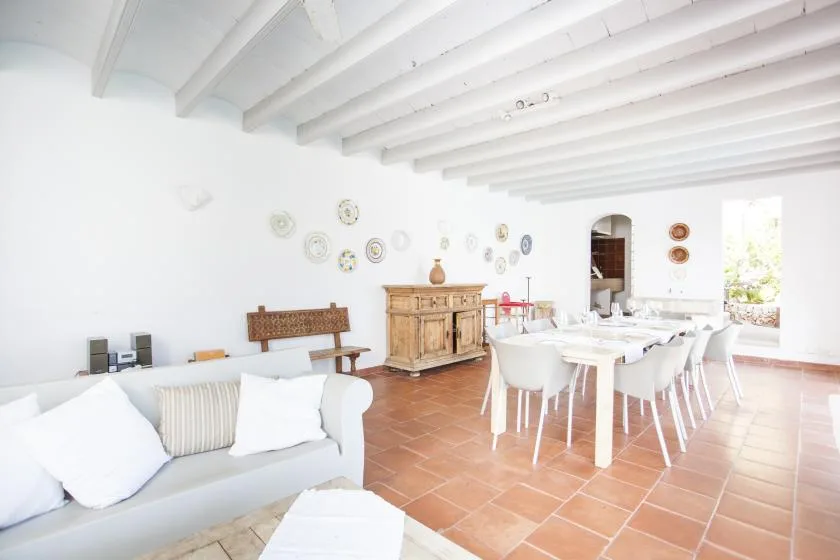 A bright dining and living area with a long table and white seating.