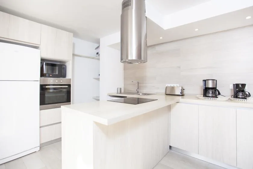 A bright modern kitchen with a central island and stainless steel range hood.
